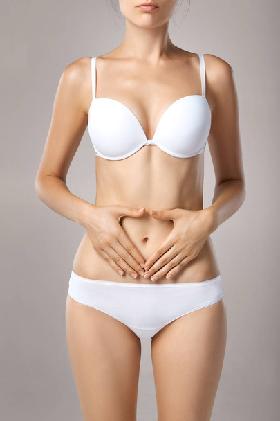 Woman health problem. Closeup of female with fit slim body in panties and bra suffering from pain and holding her hands on the stomach. Digestive disorders, period pain, health issues concept - Foto, Bild