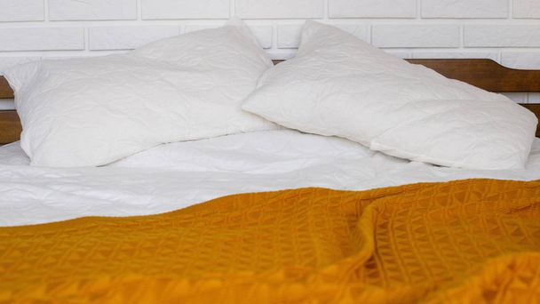 Una cama con almohadas blancas, una sábana y una manta amarilla cálida con una manta. Interior minimalista del hogar y comodidad
 - Foto, Imagen