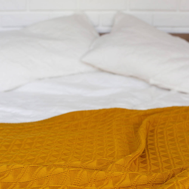 ein Bett mit weißen Kissen, ein Laken und eine gelbe warme Decke mit einer Decke. Zuhause minimalistisches Interieur und Gemütlichkeit - Foto, Bild