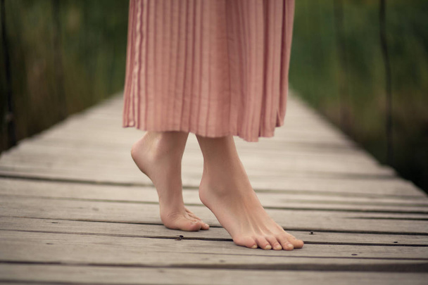 bela menina macia em um vestido de cor de pêssego andando em uma ponte de madeira rural com um buquê de flores nas mãos
. - Foto, Imagem