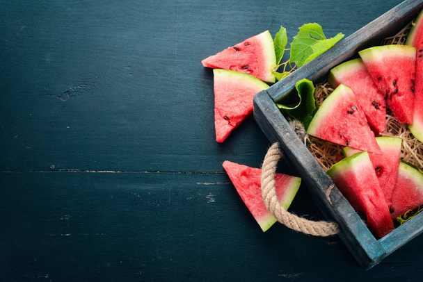 Watermelon in a wooden box. Sliced to pieces of watermelon. On a wooden background. Free space for text. Top view. - Foto, Bild