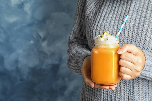 Woman in knitted sweater holding mason jar with pumpkin spice latte on color background. Space for text - Foto, Imagen