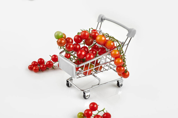 Mini shopping cart full with cherry tomatos on white background - Фото, зображення