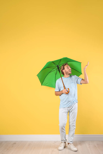 Man with green umbrella near color wall - Фото, зображення
