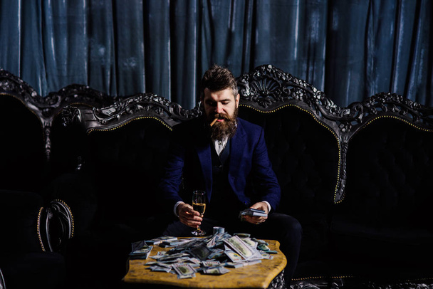 The young rich man holding whiskey glass and stack of dollars on table. - Фото, зображення