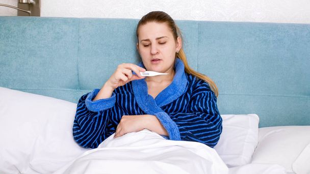 Mujer joven molesta sintiéndose enferma midiendo la temperatura con el termómetro
 - Foto, imagen