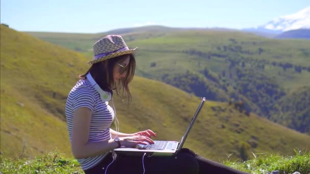 Porträt eines freiberuflichen Mädchens mit Laptop auf einer Lichtung mit Blick auf die Berge, slow mo - Filmmaterial, Video