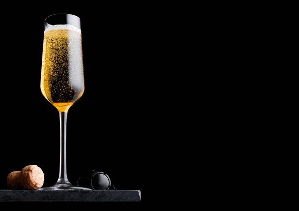 Elegant glass of yellow champagne with cork and wire cage on black marble board on black background.  - Fotoğraf, Görsel