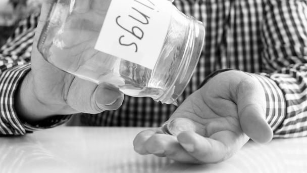 Schwarz-Weiß-Bild eines jungen Mannes, der Glas mit Ersparnissen leert - Foto, Bild