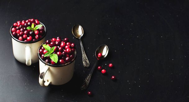 Mirtilli rossi freschi con foglie di menta in una tazza bianca e cucchiai su uno sfondo nero scuro con spazio copia. Berry, Natale sfondo vacanza
 - Foto, immagini