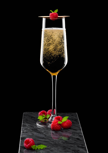 Elegant glass of yellow champagne with raspberry and fresh berries with mint leaf on stick on black marble board on black. - Foto, Imagem
