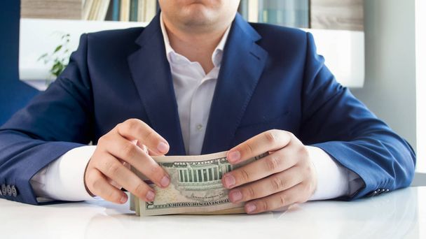 Imagen de primer plano del joven empresario exitoso sentado detrás del escritorio y sosteniendo una gran pila de dinero
 - Foto, imagen