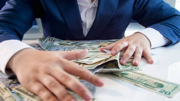 Крупним планом фото жадібного бізнесмена, який захоплює гроші лежачи на офісному столі
 - Фото, зображення