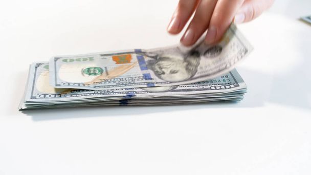 Foto de close-up de mão agarrando 100 dólares de grande pilha de dinheiro em backgorund branco
 - Foto, Imagem