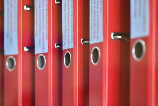 Punaiset suuret kansiot tiedostot, joissa on merkinnät toimistoasiakirjojen tallentamiseksi, seisovat pystysuorassa hyllyllä
 - Valokuva, kuva