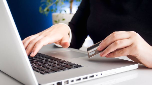Closeup image of young woman browsing internet and holding credit card in hand - Photo, image