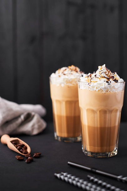 Iced caramel latte coffee in a tall glass with chocolate syrup and whipped cream. Dark wooden background with copy space. - Фото, зображення