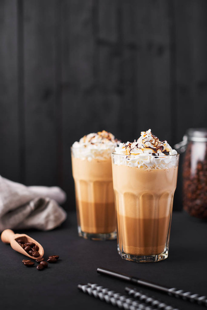 Iced caramel latte coffee in a tall glass with chocolate syrup and whipped cream. Dark wooden background with copy space. - Foto, Imagem