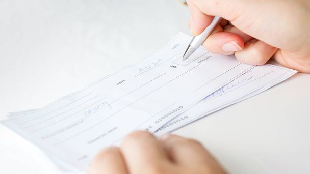 Close-up beeld van persoon vullen geld bedrag op persoonlijke bank cheque - Foto, afbeelding