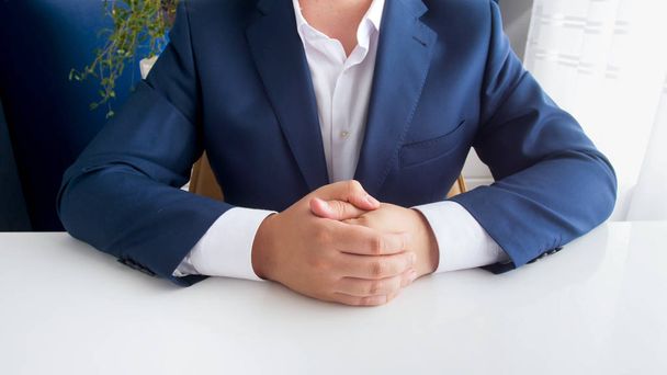 Foto de primer plano del hombre de negocios en traje azul sentado detrás de escritorio de oficina de madera blanca
 - Foto, Imagen