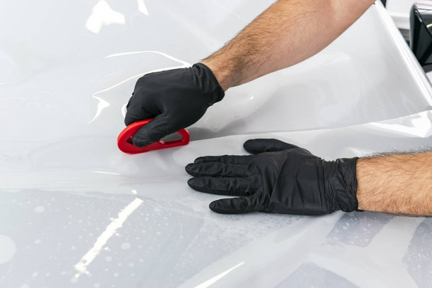 Car wrapping specialist putting vinyl foil or film on car. Protective film on the car. Applying a protective film to the car with tools for work. Car detailing. Transparent film, car paint protection. Trimming plastic soft hard squeegee - Фото, зображення