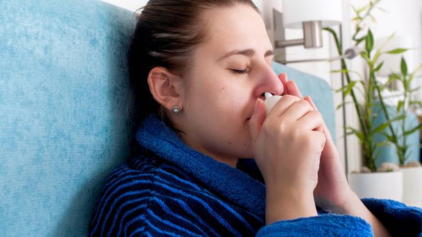 Portret zbliżenie chore kobiety złowionych zimno przy użyciu aerozolu do nosa aby zatrzymać nieżyt nosa - Zdjęcie, obraz