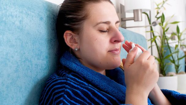 Retrato de una mujer joven que sufre de rinitis usando aerosol nasal
 - Foto, imagen