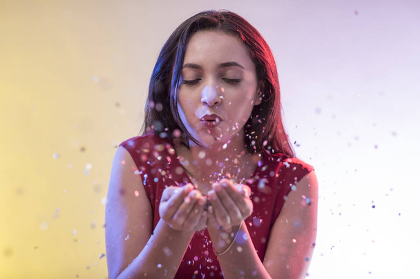Beautiful girl on party background blowing confetti - Foto, imagen