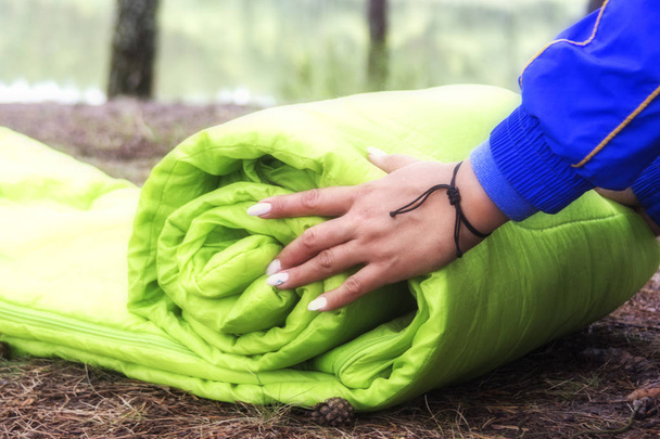 A woman folds and packs a sleeping bag, going on a journey through the forest. The concept of tourism and ecotourism. Equipment for traveling. - Foto, afbeelding