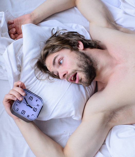 Man unshaven surprised shocked face lay pillow alarm clock top view. Toughest part of morning simply getting out of bed. Guy missed alarm clock ringing. Get up early morning tips. Oversleep again - Zdjęcie, obraz