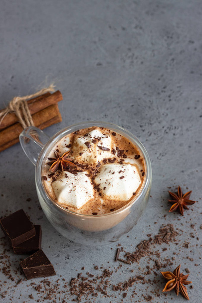 Hot chocolate cocoa drink in glass mug with marshmallows candies, cinnamon sticks, anise, chocolate and waffles. Copy space. Winter food and drink concept. - Fotó, kép