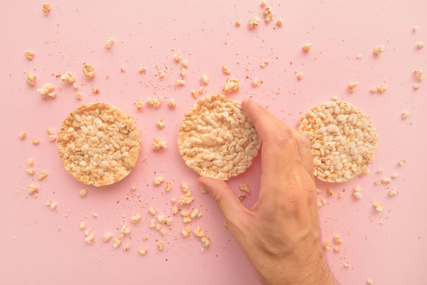 Rice cakes in male hand over pastel pink background, overhead view - Foto, imagen