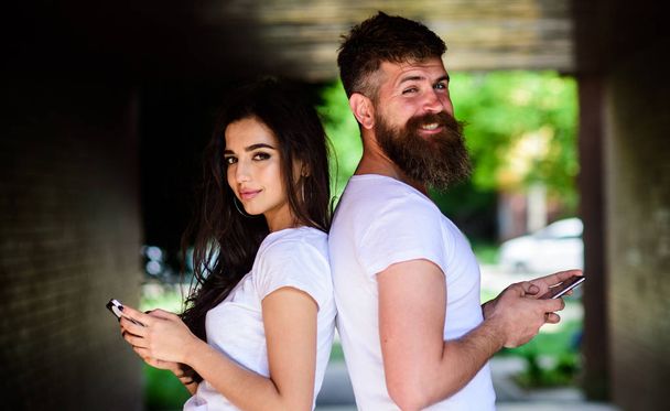 Couple ignore real communication. Couple chatting smartphones. Girl and bearded man stand back to back porch or underground. Virtual cheating online. Suspect in cheating. Send provocative message - Foto, afbeelding