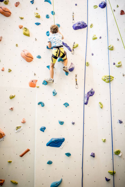 closeup of young boy hanging on a rope leading to the top of an artificial climbing wall, personal development and career growth or challenge yourself concept - Photo, image