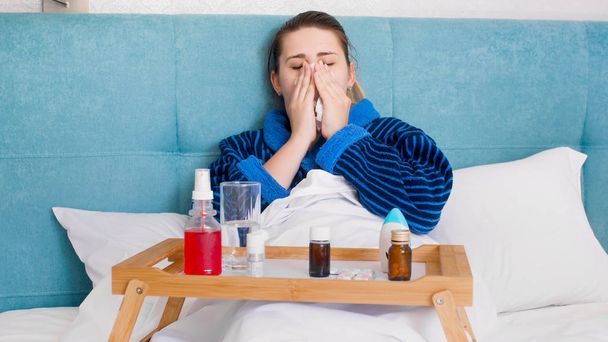 Portrét nemocná s rýma, ležící v posteli a smrkání v ubrousek - Fotografie, Obrázek