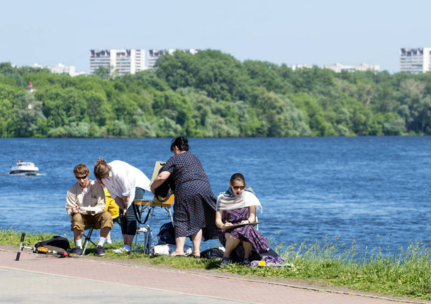2018.05.27, Moscow, Russia. A group of painters sitting on the river embankment. A group of creative people in the park on river background. - 写真・画像
