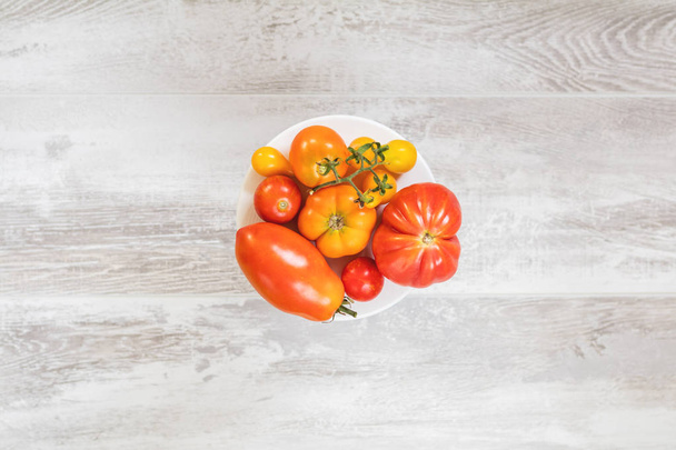 Veel verschillende rode oranje gele tomaten op lichte houten oppervlak. Mooie voedsel kunst achtergrond, bovenaanzicht. - Foto, afbeelding
