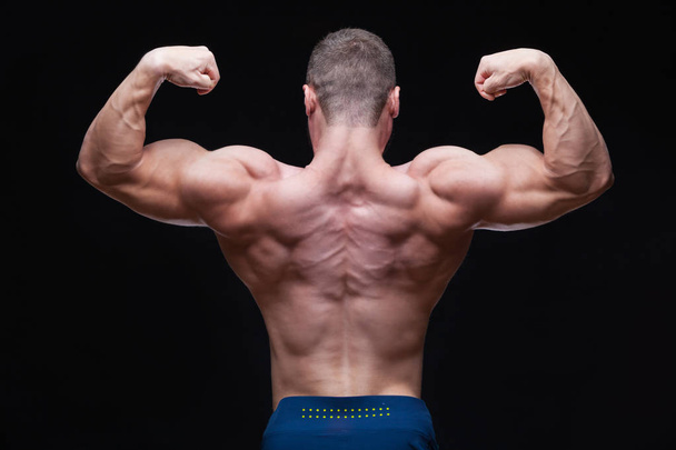 Rear view of healthy muscular young man with arms bent out isolated on black background - Fotoğraf, Görsel