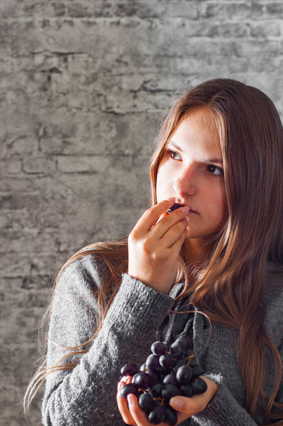 ritratto di giovane adolescente ragazza bruna con i capelli lunghi mangiare uva su sfondo grigio parete
 - Foto, immagini
