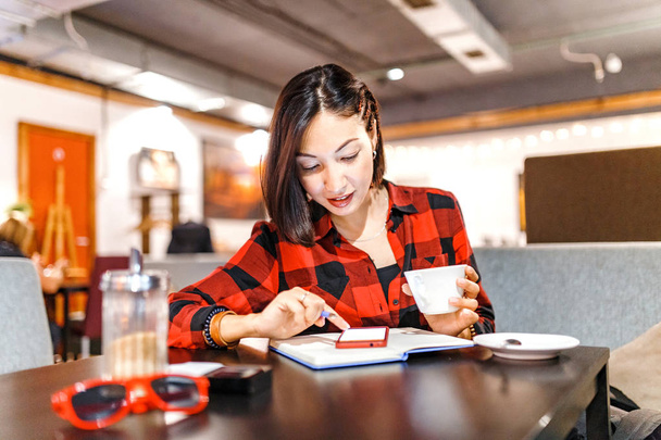 Joven bonita morena hipster feliz chica usando teléfono inteligente sentado con café en la cafetería
 - Foto, Imagen