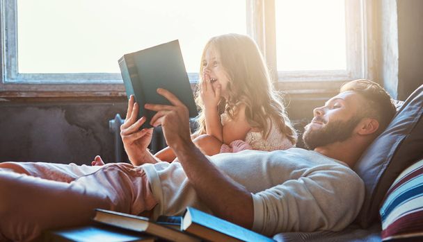 Pohledný mladý otec čtení pohádky svou malou dceru na posteli. - Fotografie, Obrázek