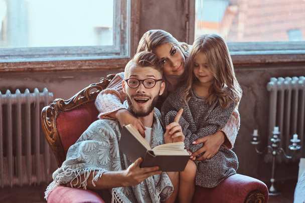 Family togetherness. Mom, dad and daughter reading story book together sitting on the couch. Family and Parenthood Concept. - Foto, Imagem