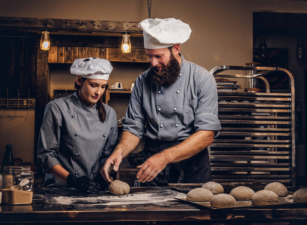 Chef enseñando a su asistente a hornear el pan en una panadería
. - Foto, Imagen