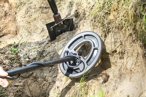 Metal detector coil over a metal object protruding from the ground. A shovel driven into the ground in the background. - Photo, Image