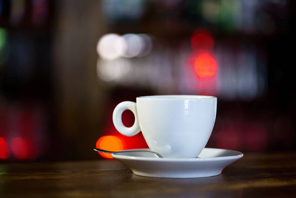 a white mug with a saucer and a spoon is on a wooden table in a restaurant. Close-up - Foto, Imagem