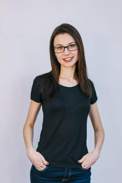young girl in glasses is dressed in a black T-shirt and blue jeans stands on a white background - Foto, Imagem