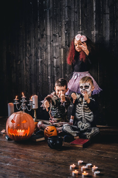 Groep van schattige multiraciale kids in enge kostuums tijdens Halloween party in een oud huis. - Foto, afbeelding