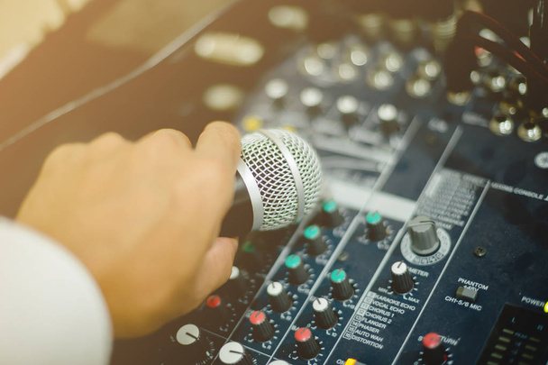 Micrófono en la mano y ajuste un controlador de mezclador de audio en la sala de control, control de mezclador de sonido para música en vivo y equipos de estudio, sistema de audio de calidad para profesionales, concepto de equipo de música
. - Foto, Imagen
