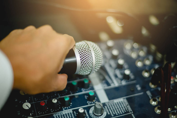 Microfoon in hand en aanpassen van een audio mixer-controller in de controlekamer, Sound mixer control voor live muziek en studio apparatuur, kwaliteit audio systeem voor professionals, muziek apparatuur concept. - Foto, afbeelding