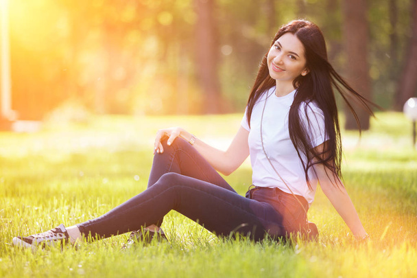 Nuori nainen rentoutuu puistossa vihreällä ruoholla. Kauneus luonto kohtaus värikäs tausta, puita kesäkaudella. Ulkoilmaelämää. Onnellinen hymyilevä nainen istuu vihreällä ruoholla - Valokuva, kuva